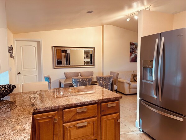 A modern kitchen with a granite countertop, wooden cabinets, a stainless steel refrigerator, and a dining area with a sofa and chairs. - Location! 10 minutes drive to Siesta Beach (Sarasota)