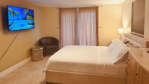 Une chambre d’hôtel avec un lit, une chaise, un téléviseur fixé au mur, une lampe et une fenêtre avec des stores.