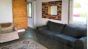 A living room with a gray sofa, a beige armchair, a wooden sliding door, a patterned rug, and a wall art piece. - Private farm house lock off on sheep farm with salt hot tub (Driggs)
