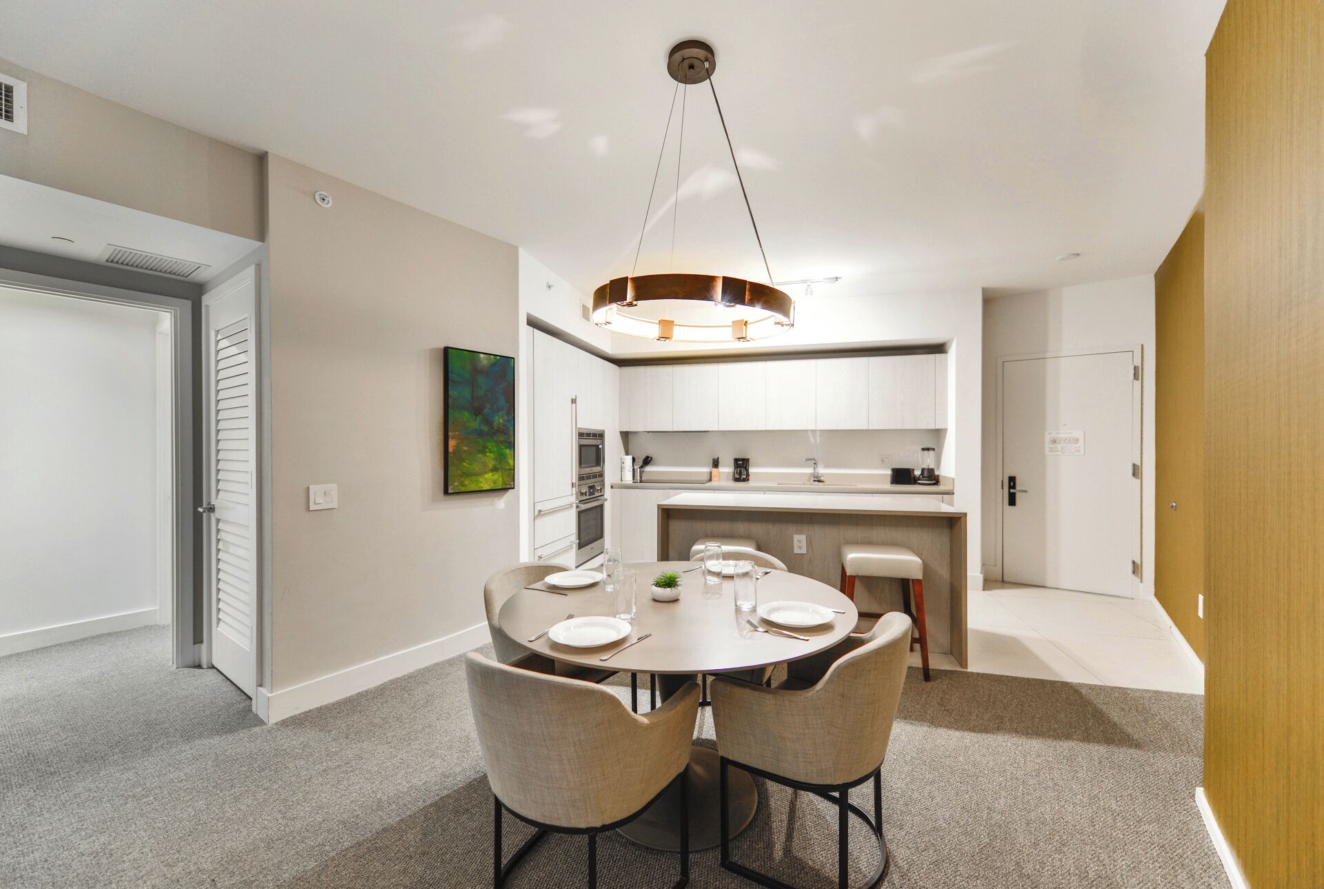 A modern kitchen with white cabinets, a central island, and a dining area with a round table and four chairs.