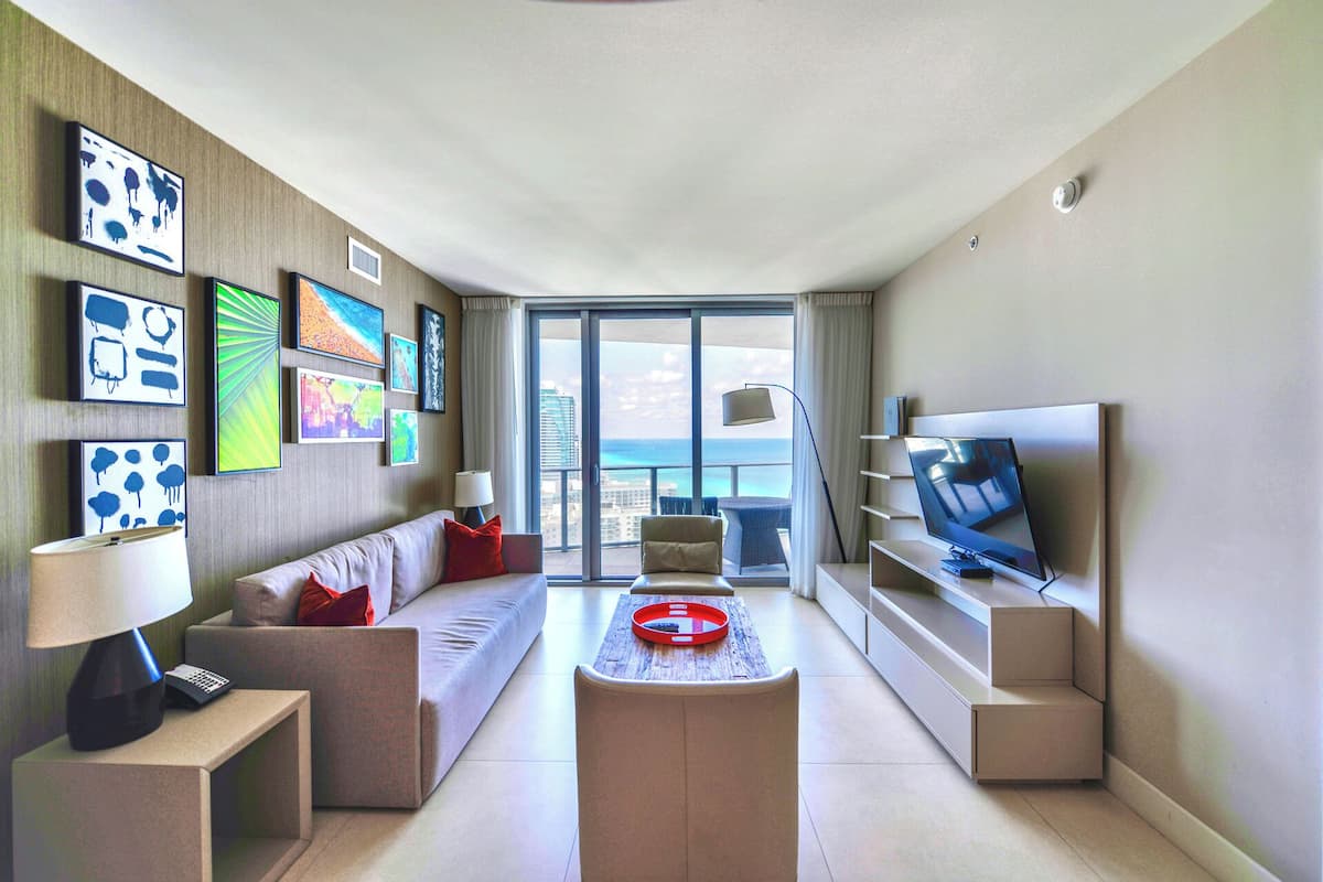 A modern hotel room with a sofa, a coffee table, a TV, and artwork on the walls.