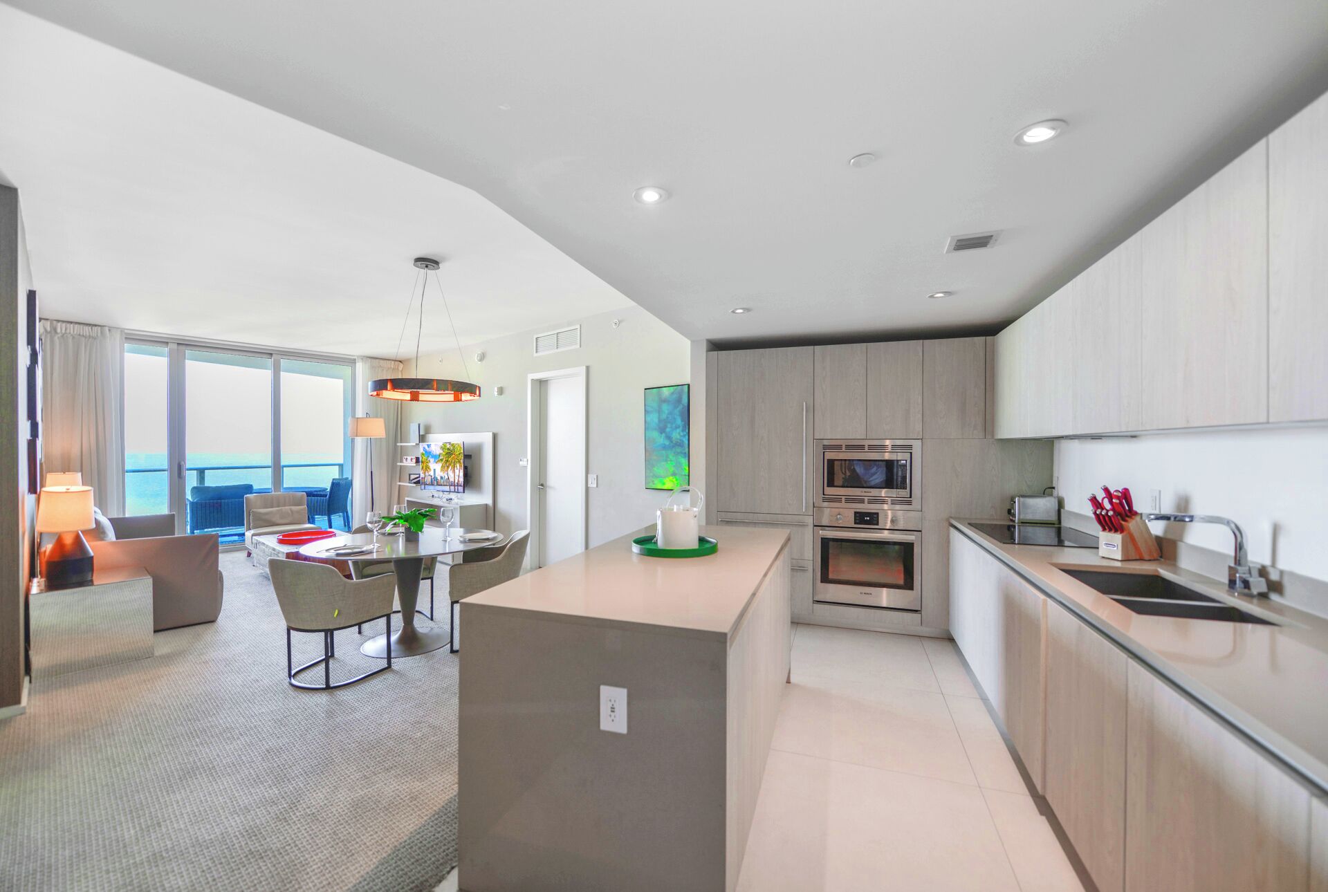 A modern hotel room with a dining area, kitchen, and a balcony with a view.