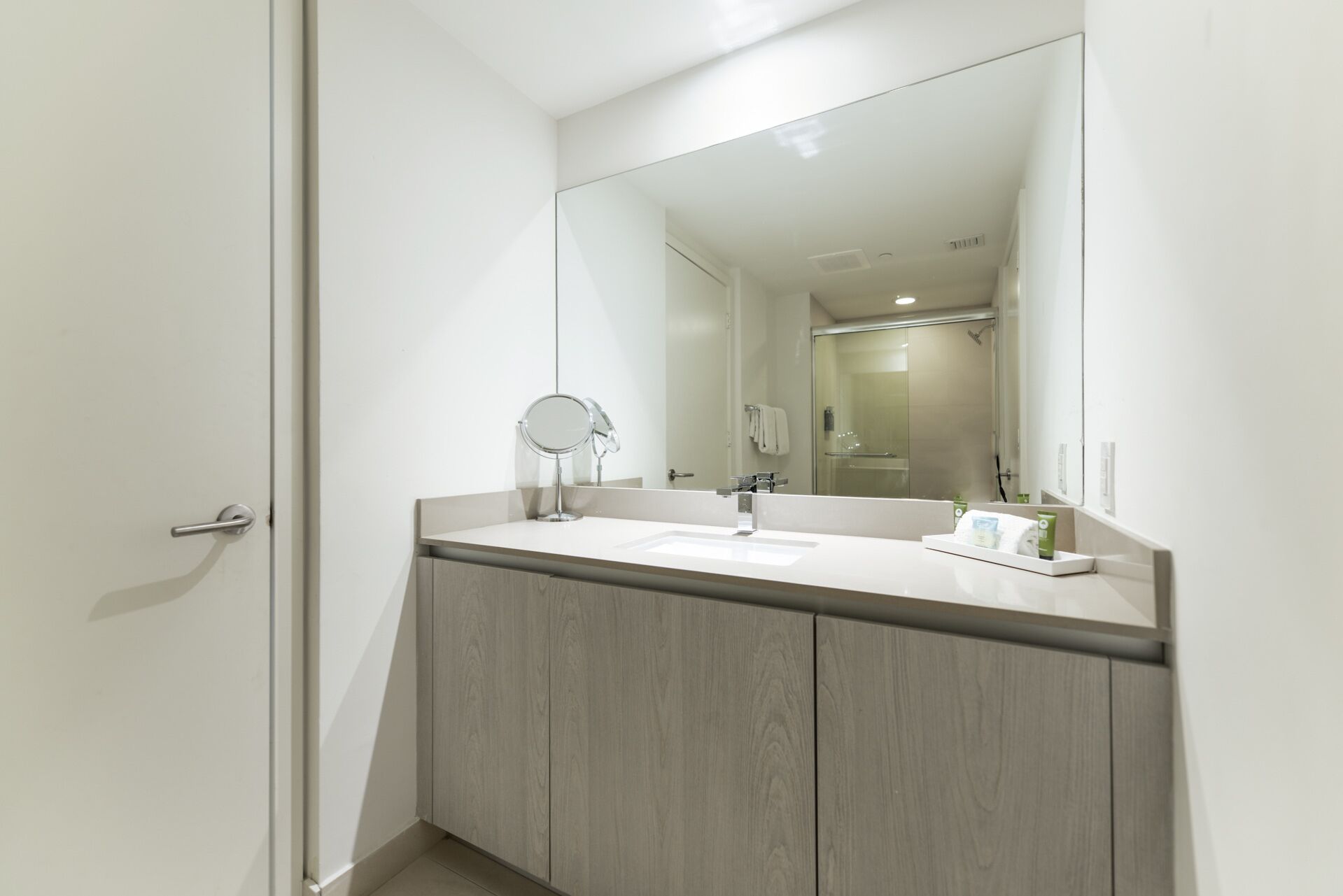 Un baño moderno con un espejo grande, dos lavamanos y armarios de madera.