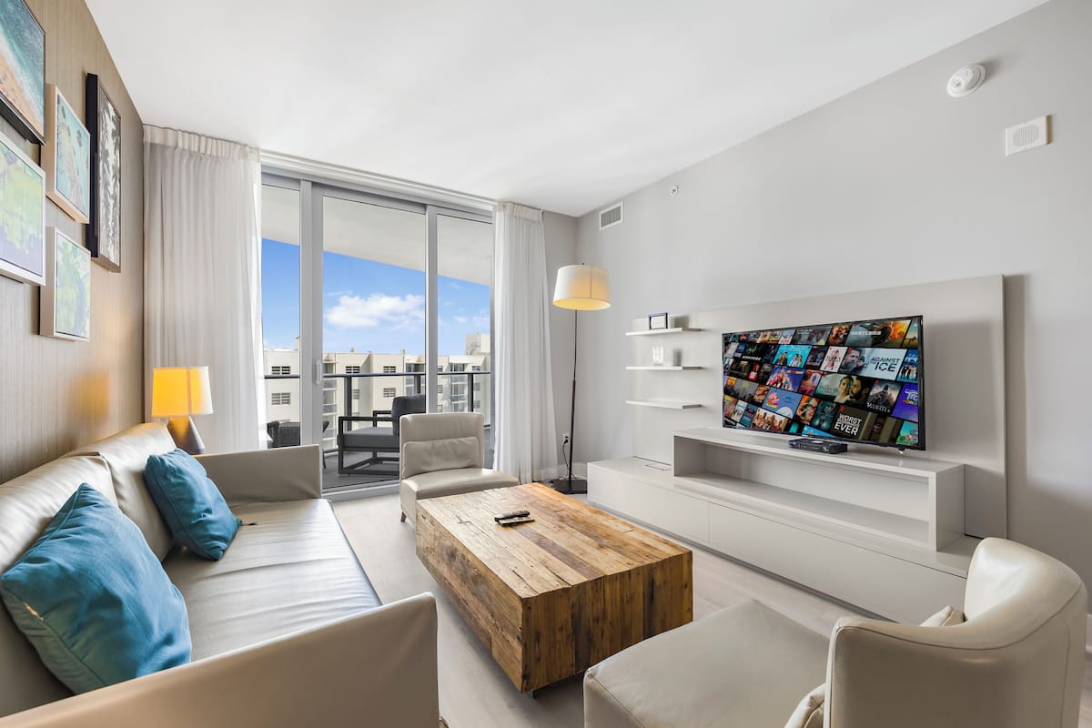 A modern hotel room with a large TV, a wooden coffee table, and a sofa with blue cushions.
