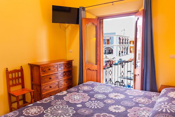 A bedroom with a bed, wooden dresser, and a chair. It has a window with a view of buildings outside. - Hotel del Parque Naolinco (Naolinco)