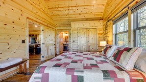 A log cabin bedroom with a large bed, wooden walls, and a view of the outdoors through large windows. - Mountain View & Fire Pit: Updated Murphy Cabin! (Murphy)