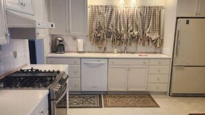 Une cuisine avec des meubles blancs, une cuisinière, un lave-vaisselle et un réfrigérateur.