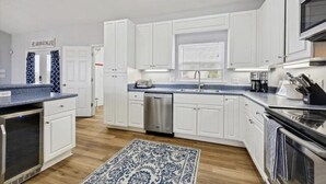 Una cucina moderna con mobili bianchi, elettrodomestici in acciaio inossidabile e un tappeto azzurro con motivo.
