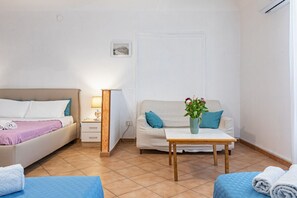 A bedroom with a bed, bedside table, lamp, and a sofa with a vase of flowers.