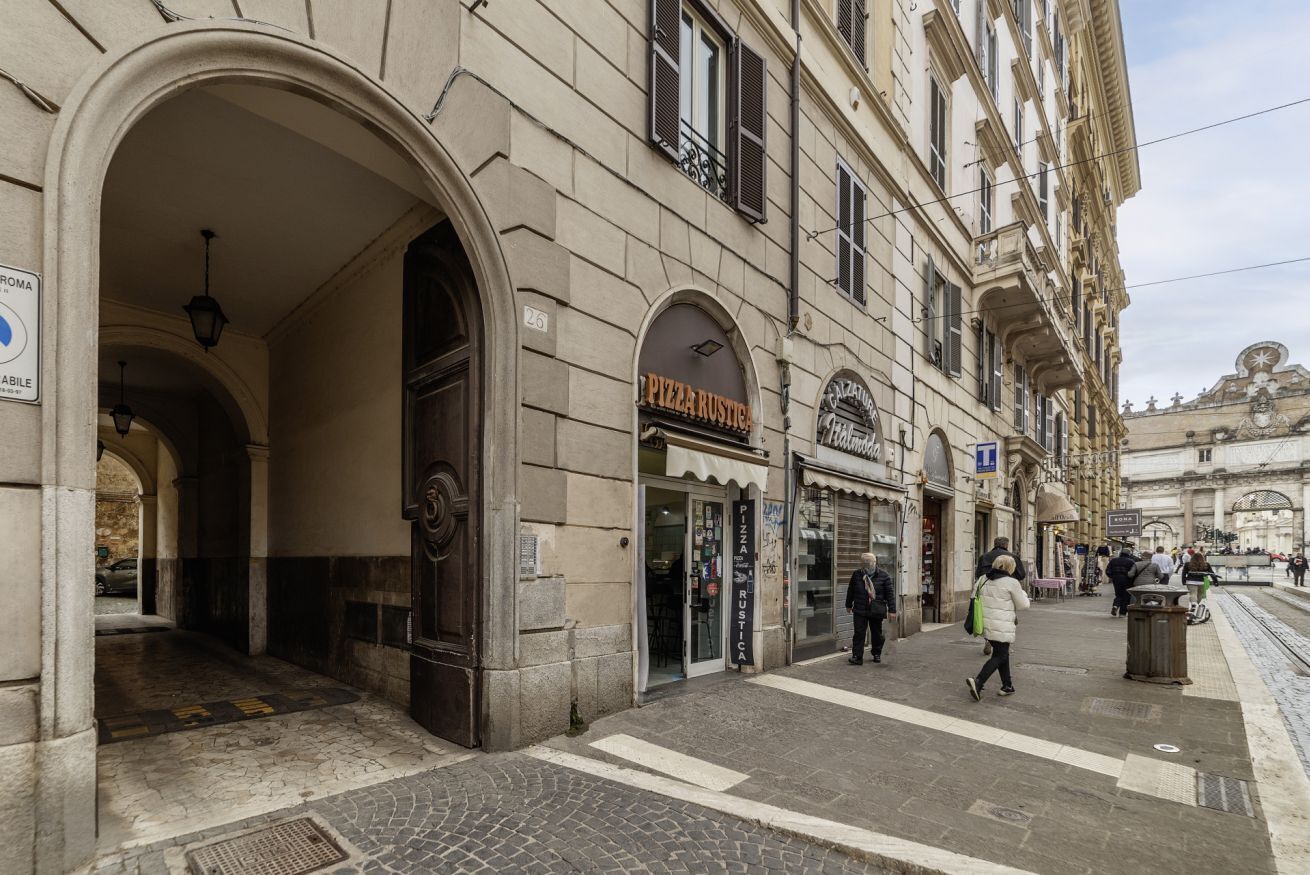 Un edificio histórico con una entrada abovedada, un restaurante de pizza y una parada de tranvía.