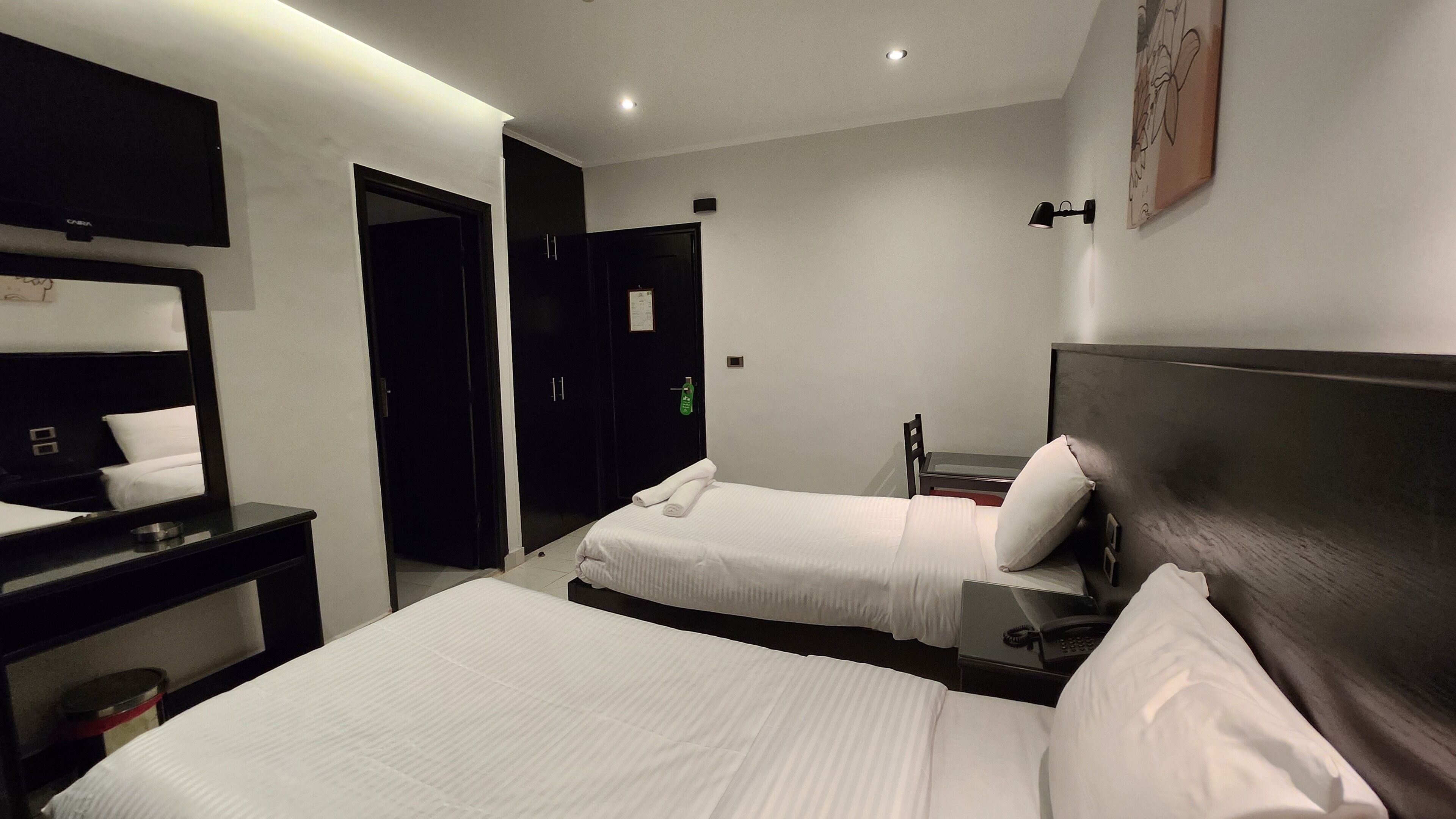 Habitación de hotel con dos camas, un escritorio, una silla, un espejo y una lámpara fijada a la pared.