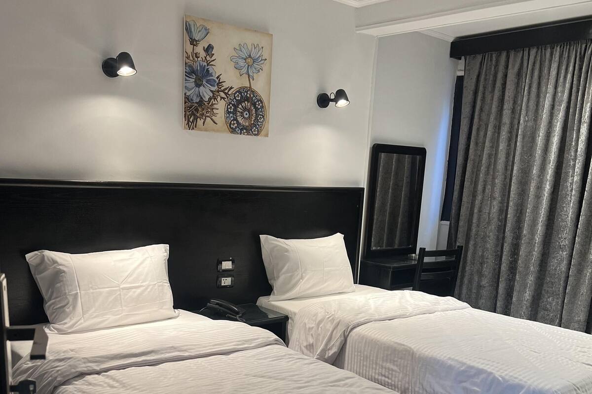 Una habitación de hotel con dos camas, un cuadro en la pared y un ventanal con cortinas.