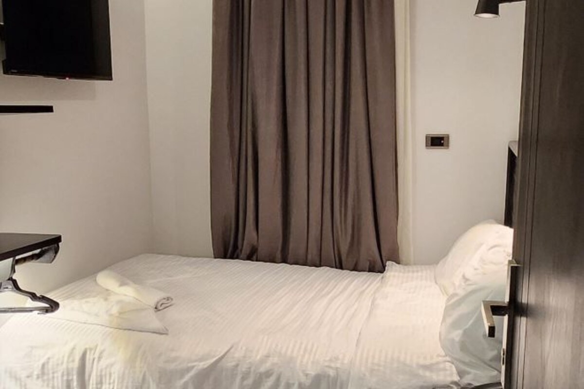 A hotel room with a bed, a flat-screen TV mounted on the wall, and a door with a handle.