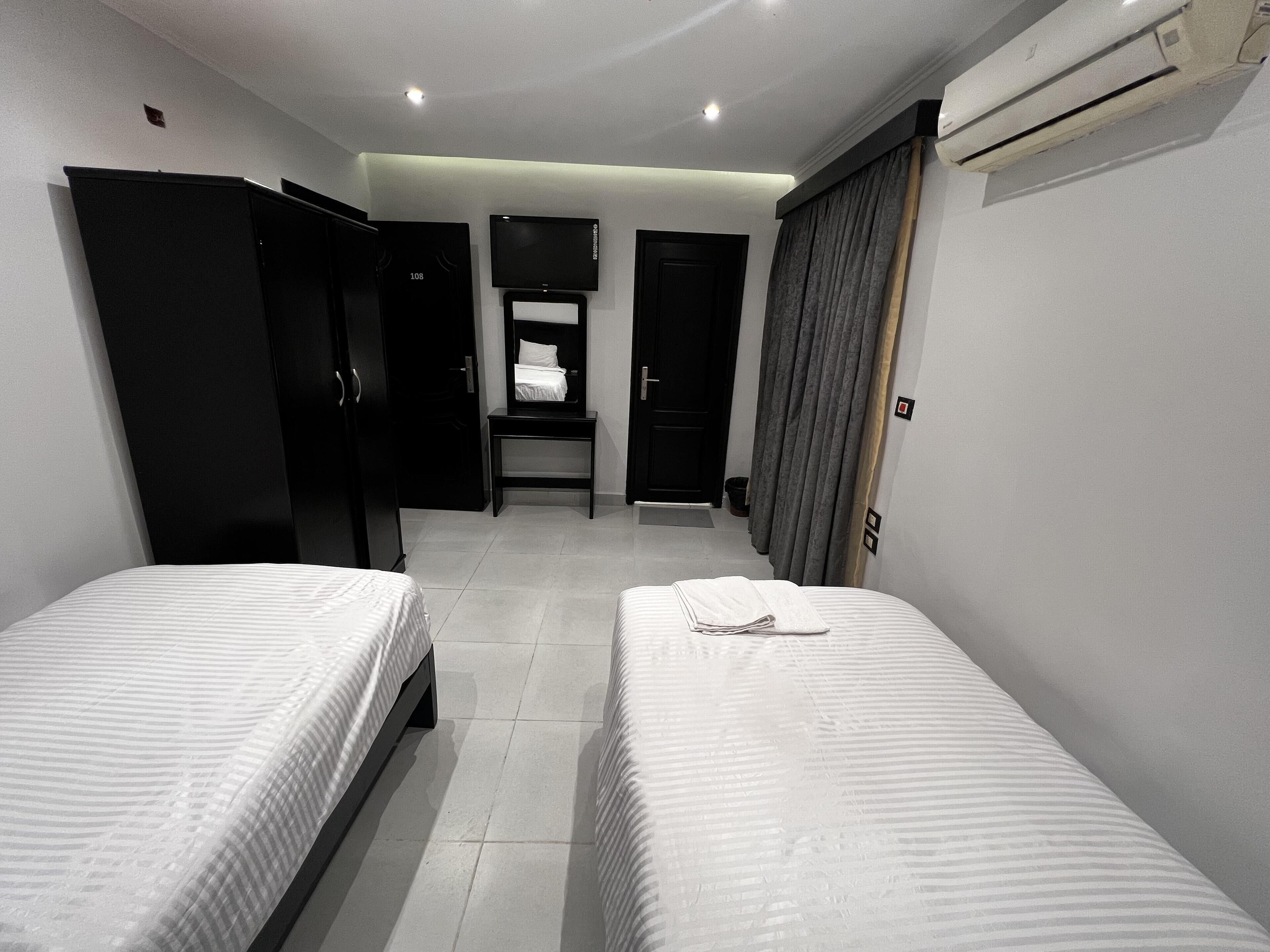 Habitación de hotel con dos camas, televisor, armario y aire acondicionado.