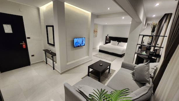 Ein modernes Hotelzimmer mit Sofa, Couchtisch, Fernseher, Bett und kleinem Schreibtisch.