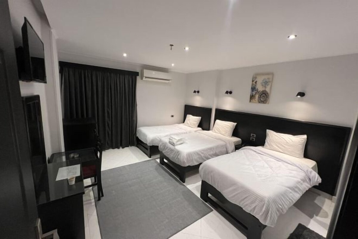 A hotel room with two single beds, a desk, a chair, a TV, and an air conditioning unit.
