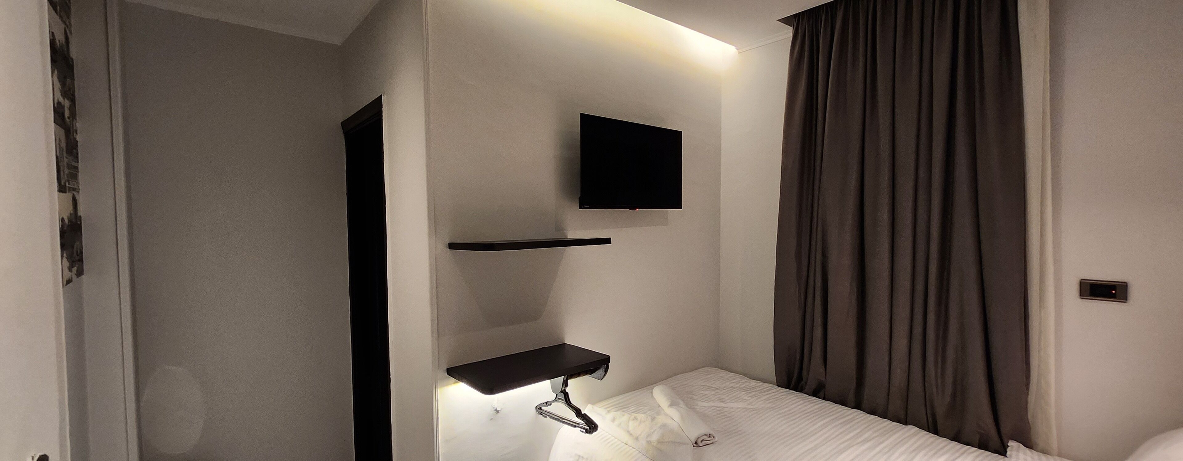 A modern hotel room with a bed, a mounted TV, and a small shelf.