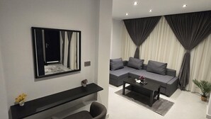 Ein modernes Wohnzimmer mit einem grauen Sofa, einem schwarzen Couchtisch, einer schwarzen TV-Konsole und einem Spiegel an der Wand.