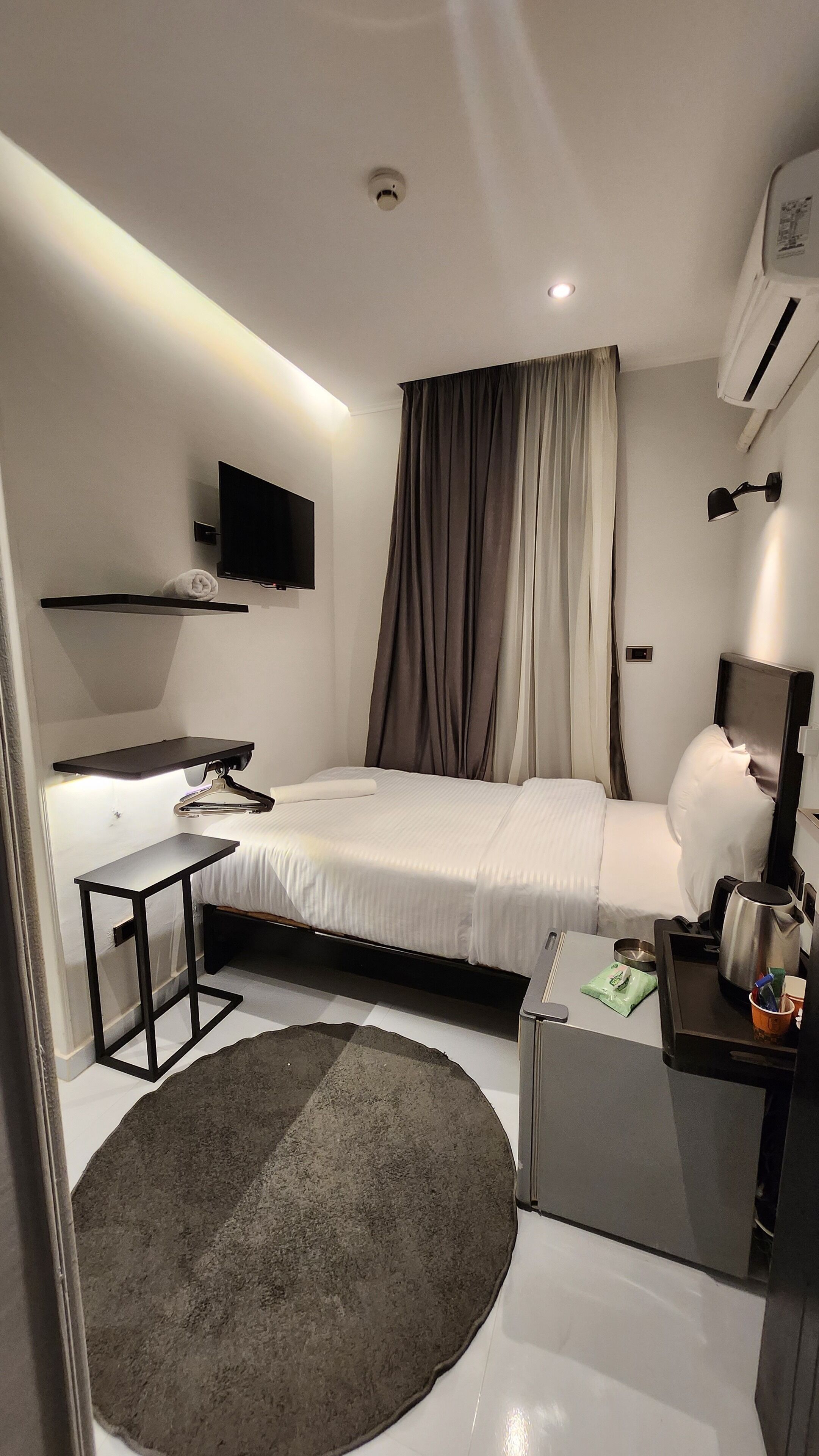 A modern hotel room with a bed, a desk, a flat-screen TV, a coffee machine, and a small rug.