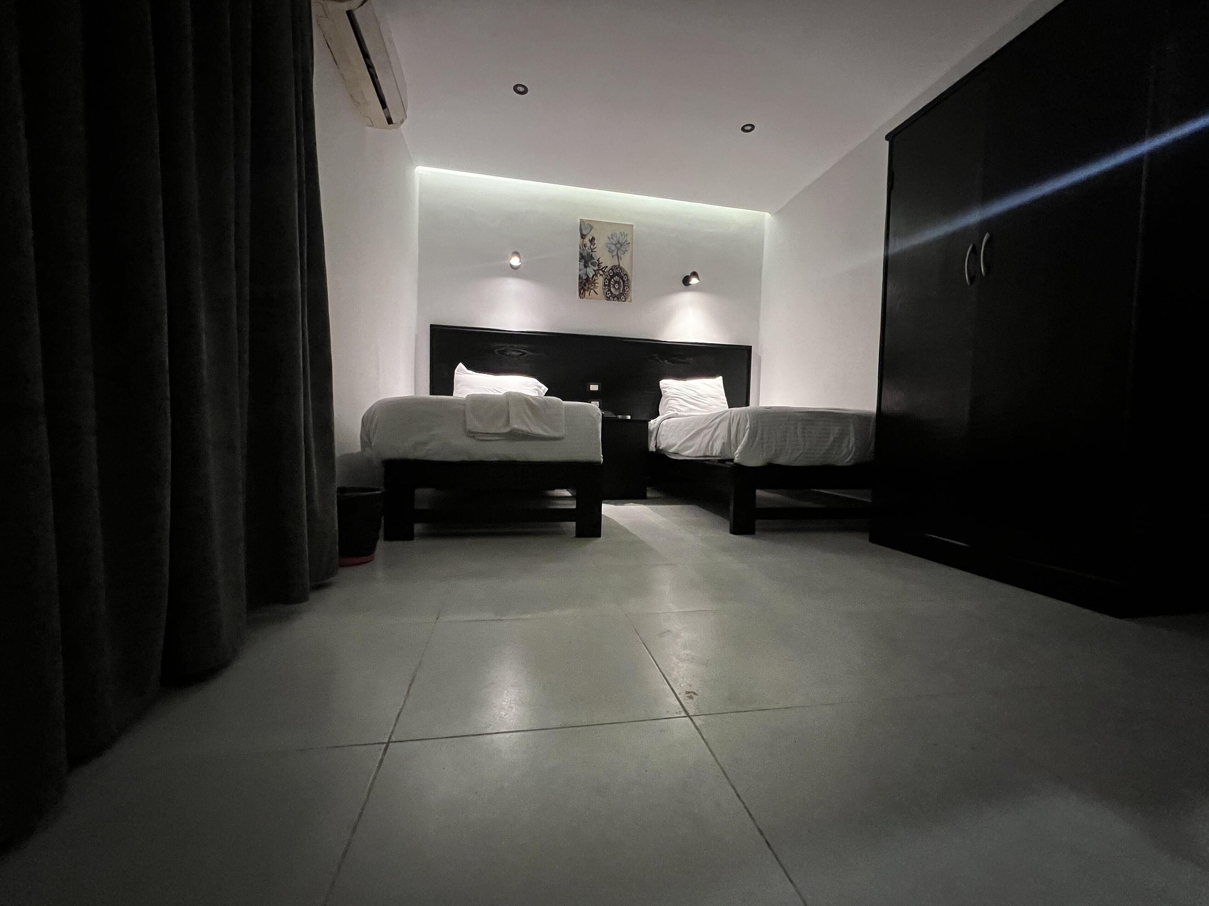 A bedroom with two beds, a dark wardrobe, and a ceiling light.