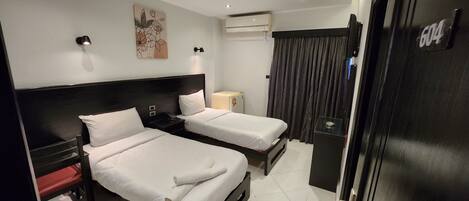 Habitación de hotel con dos camas, una mesita de noche, una pequeña mesa, un equipo de aire acondicionado y una puerta con un número.