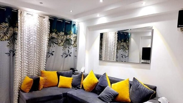 A modern living room with a sectional sofa, a large mirror, and patterned curtains. - Very nice apartment in the heart of Alexandria (Alexandria Governorate)