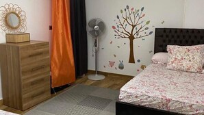 A bedroom with a bed, a dresser, a standing fan, a decorative mirror, and a wall decal. - Very nice apartment in the heart of Alexandria (Alexandria Governorate)