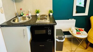 Una cocina compacta con un lavamanos, estufa y una pequeña encimera. Hay plantas en macetas sobre la encimera y una mesa pequeña con objetos encima.