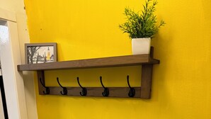 Una estantería de madera con ganchos y una planta en maceta frente a una pared amarilla.