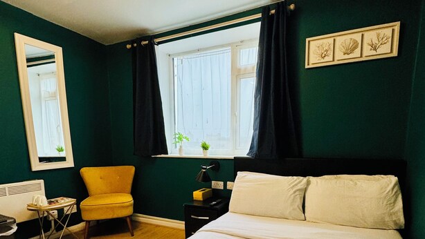 Un dormitorio ordenado con cama, una silla, una mesita de noche y una ventana con cortinas.