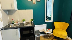 Cocina compacta con lavaplatos, estufa y lavabo, una mesa pequeña con una silla, y ventana con vistas.