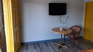 Une pièce avec un plancher en bois, une table ronde avec une chaise, un téléviseur fixé au mur et une porte portant un numéro.