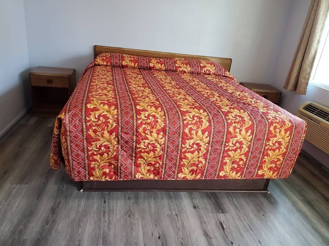 A bedroom with a wooden bed, a nightstand, a bedside table, and a window with curtains.