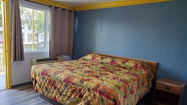 Une chambre à coucher avec un lit, une fenêtre avec des rideaux, une table de chevet et un mur orné d’une bordure jaune.