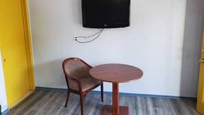 Une pièce avec un téléviseur fixé au mur, une chaise en bois et une petite table ronde.