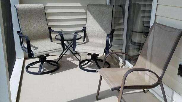 Ein überdachter Patio-Bereich mit vier Stühlen und einem Tisch, der einen Blick auf die Außenansicht des Hauses bietet.