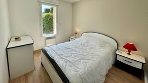 Une chambre à coucher avec un lit, des tables de chevet, une fenêtre et un radiateur.