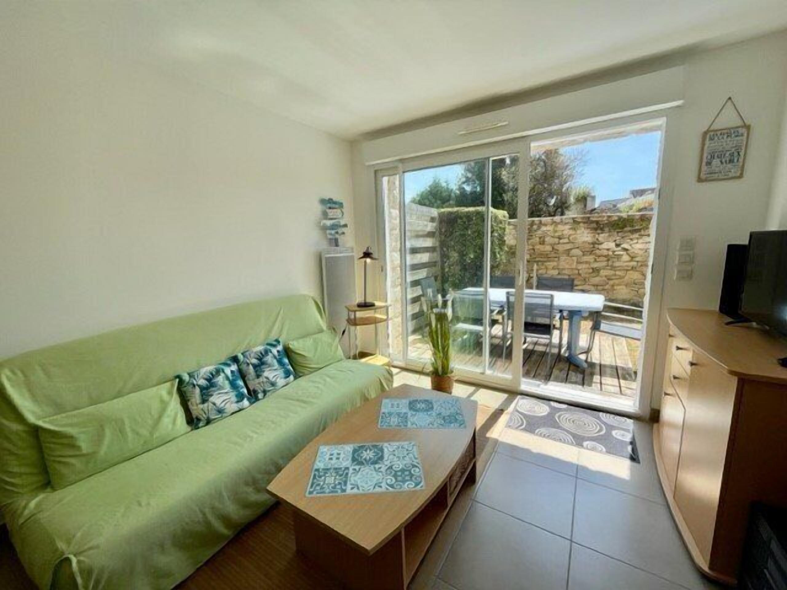 Ein Wohnzimmer mit einem grünen Sofa, einem Holztisch und einer Glasschiebetür, die auf eine Terrasse mit Steinwand und Tisch führt.