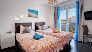 A hotel room with two beds, a TV, a balcony, and a view of the outside.