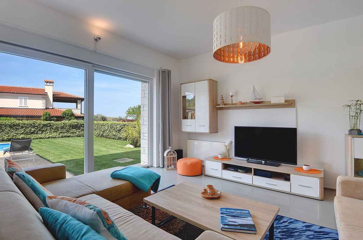 A modern living room with a large TV, comfortable seating, and a view of the garden.