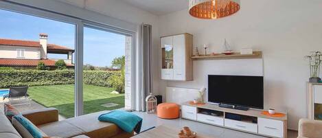A modern living room with a large TV, comfortable seating, and a view of the garden.