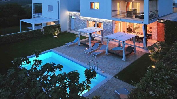 A modern two-story house with a swimming pool, outdoor seating, and a well-lit patio area.
