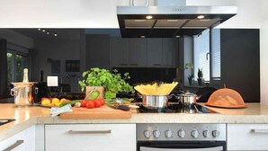 A modern kitchen with a stainless steel range hood, a built-in oven, and a countertop with fresh vegetables and cooking utensils.