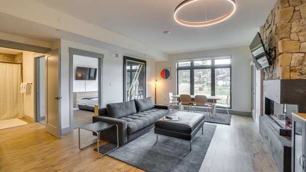 A modern living room with a grey sofa, a coffee table, and a fireplace. There is a TV mounted on the wall and a window providing natural light. - Modern Winter Park Condo w/ Community Hot Tub! (Winter Park)