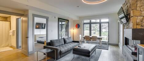 Un salon moderne avec un canapé gris, une table basse et une cheminée. Un téléviseur est fixé au mur et une fenêtre laisse entrer la lumière naturelle.