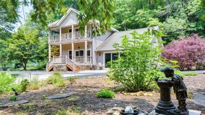 A two-story house with a balcony, surrounded by a garden with various plants and a statue. - Riverfront Hayesville Retreat: Fishing & Kayaking! (Hayesville)
