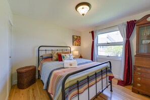 Una camera da letto con un letto, una cassettiera, una finestra con tende, una lampada e un'opera d'arte appesa al muro.