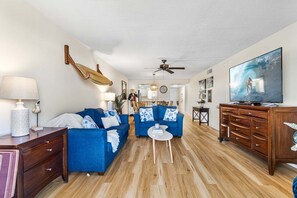 Un salon avec deux canapés bleus, un meuble en bois, une télévision et un ventilateur de plafond.