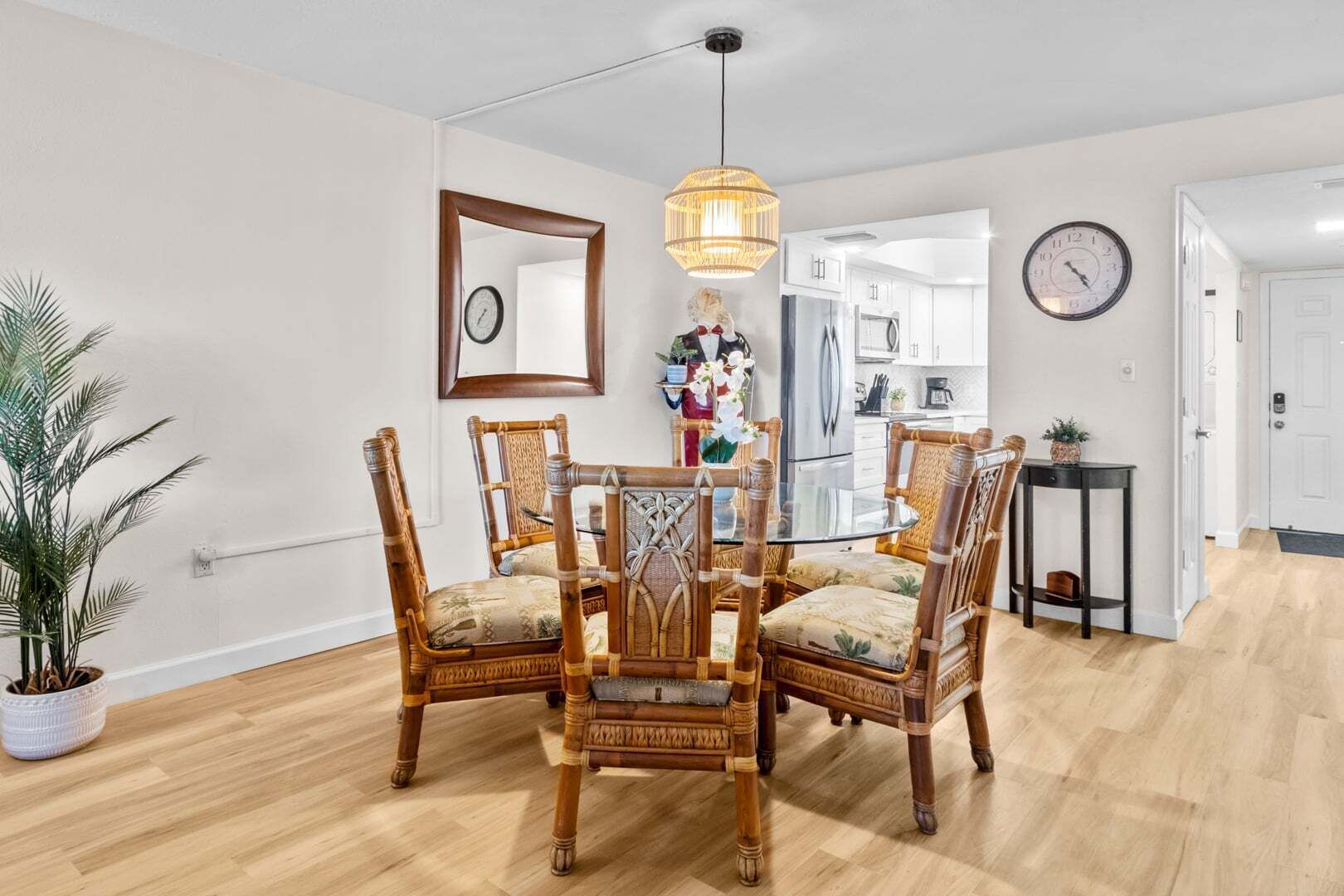 Un coin repas avec une table ronde en verre entourée de quatre chaises, un luminaire suspendu, une horloge et une plante en pot.
