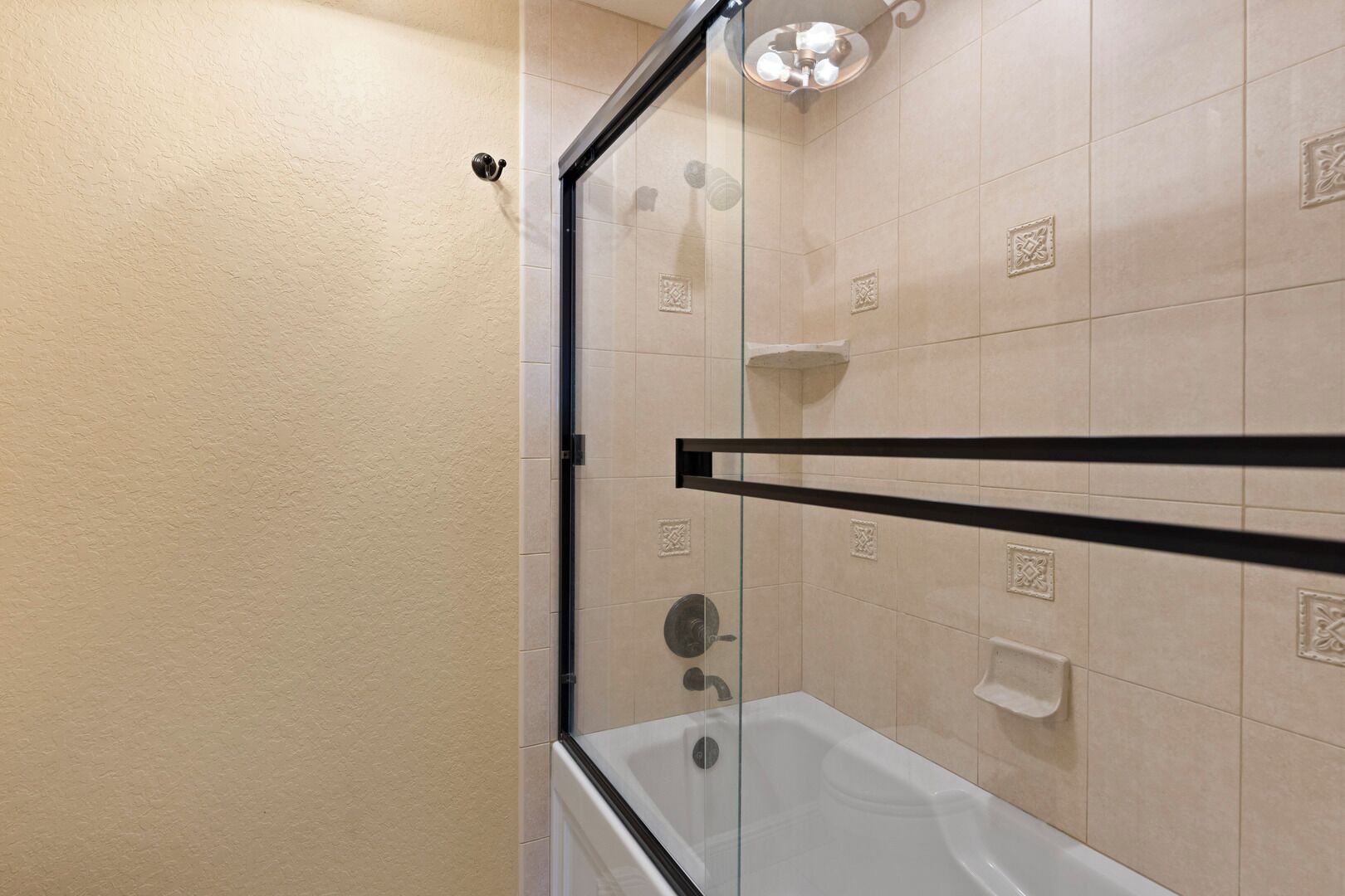 A modern bathroom with a glass-enclosed shower, a white bathtub, and beige tiled walls.